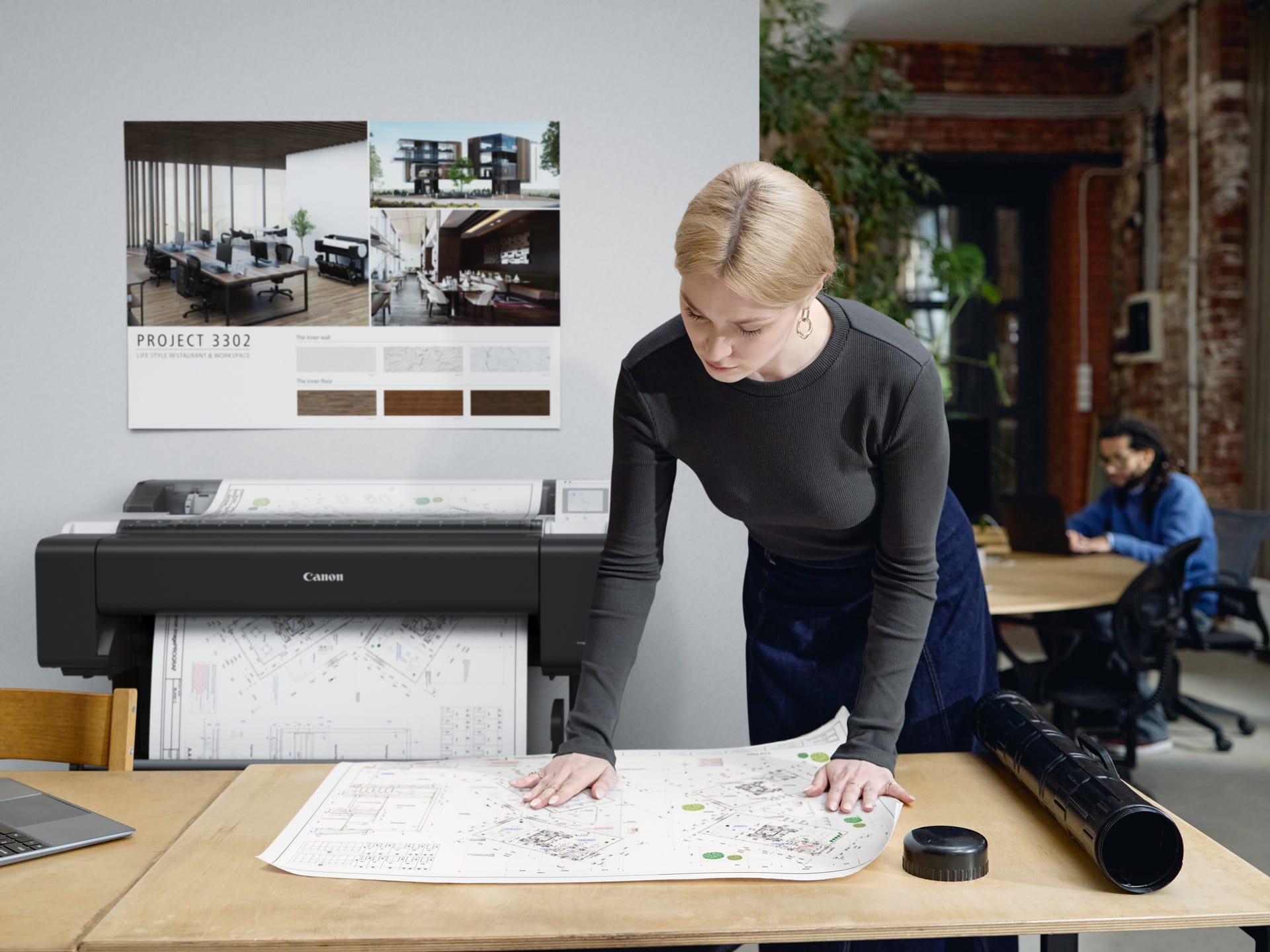 Architect reviewing a printed site plan beside a Canon imagePROGRAF TM-610M A0 multifunction printer
