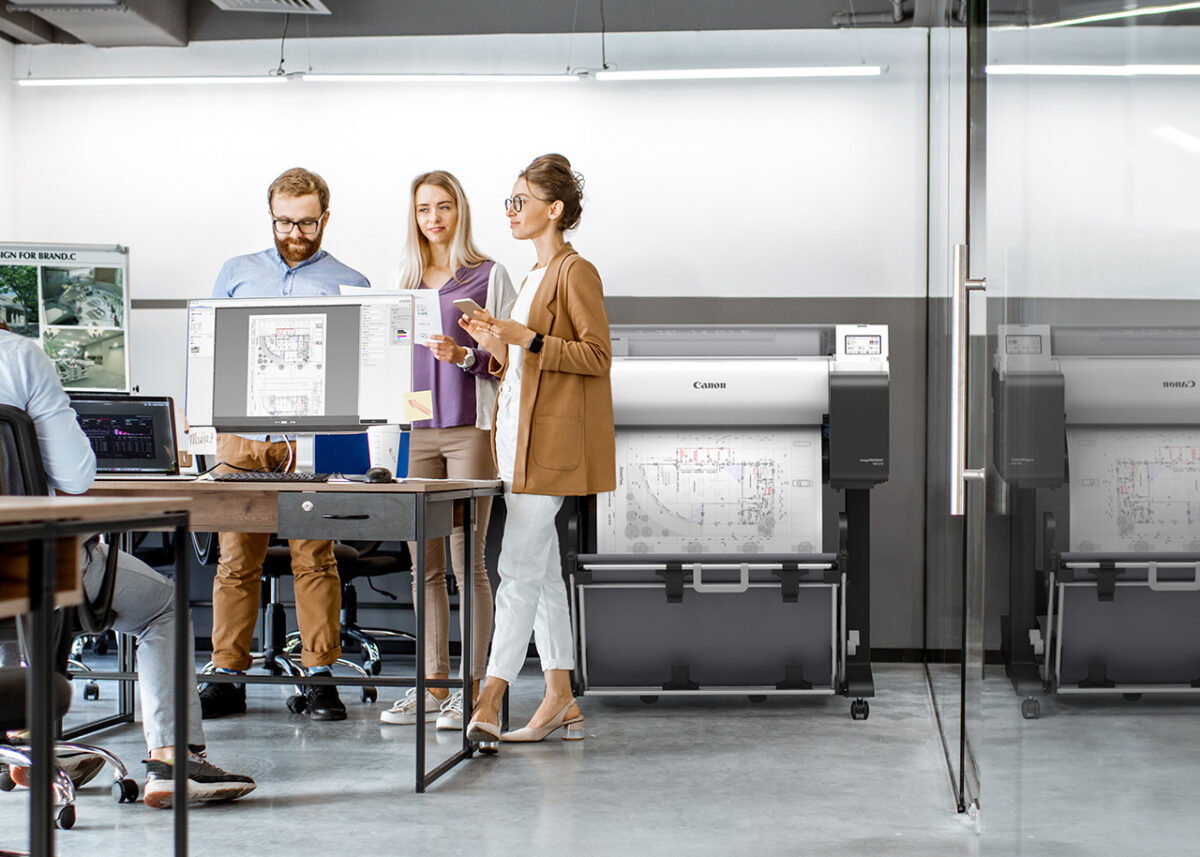 Design office team reviewing a floor plan beside two Canon imagePROGRAF TM-510 A1 plotters printing technical drawings