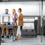 Design office team reviewing a floor plan beside two Canon imagePROGRAF TM-510 A1 plotters printing technical drawings